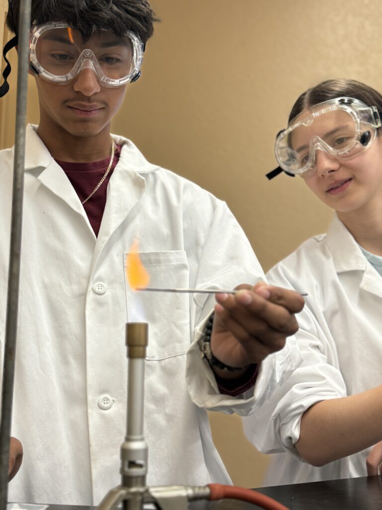 Students in lab coats conduct admissions experiment with flame.